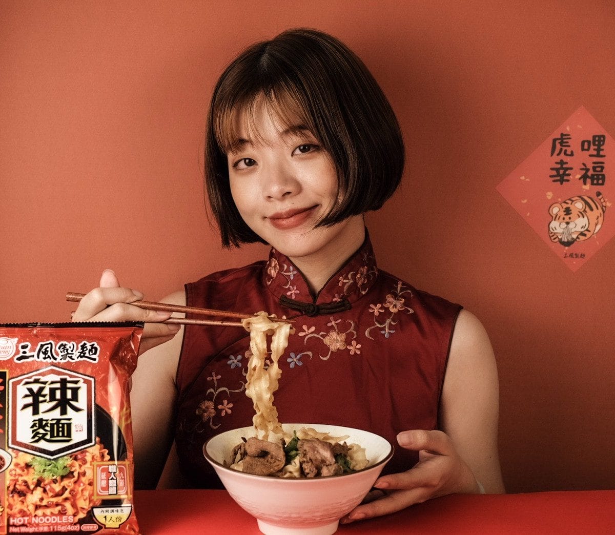 穿著旗袍的女子，帶著微笑捧著一碗乾拌麵