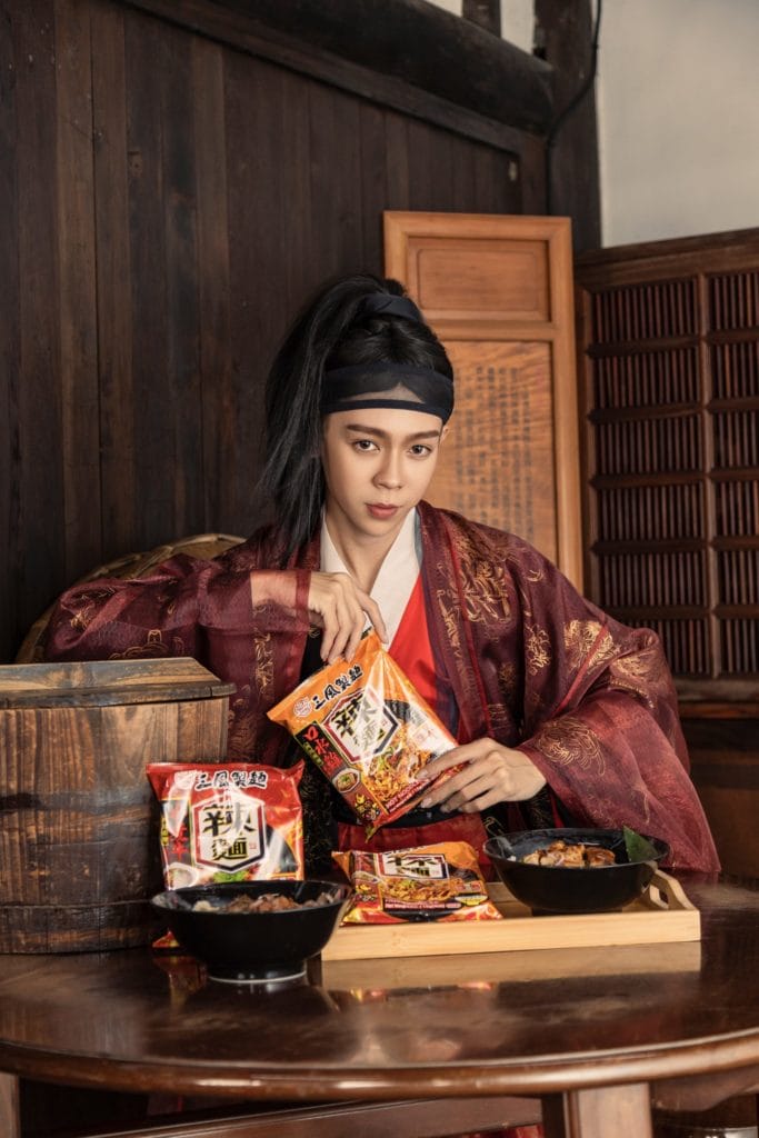 古裝男子坐在古色古香的環境中，桌上擺著乾拌麵