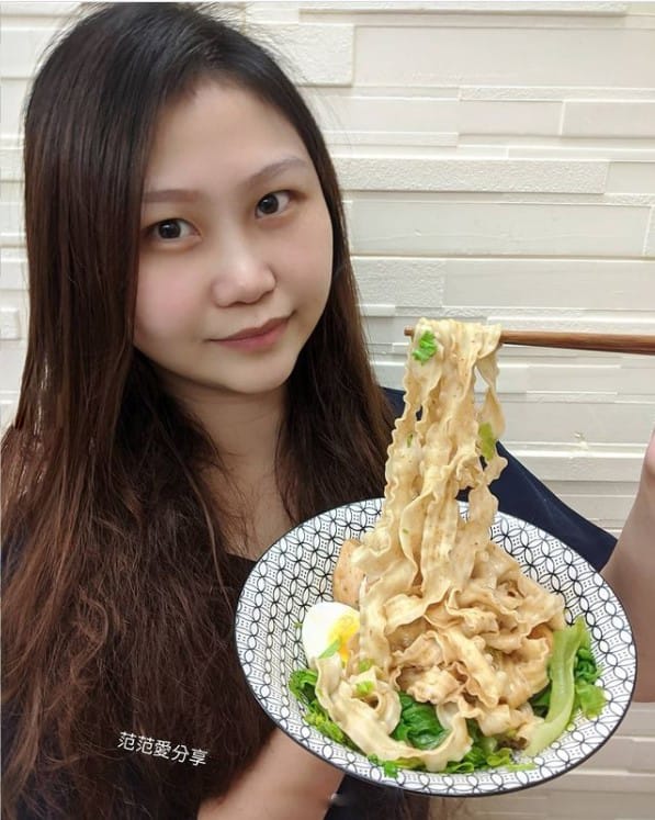 一個女子捧著乾拌麵，展示這碗麵的麵條