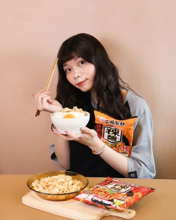一名女子展示手上的的乾拌麵，桌上散落乾拌麵的包裝